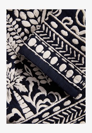 Marine stof met ingewikkelde witte borduursels met bloem- en geometrische patronen, die textuursteken en gelaagde ontwerpelementen tonen.