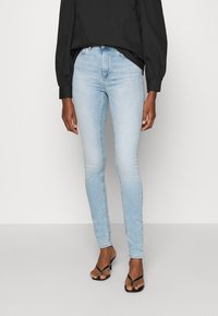 Ljust blå denim skinny jeans med hög midja, subtil blekning och en klassisk femficksdesign. Bärs med en svart topp och sandaler.