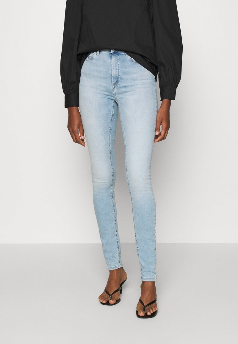 Ljust blå denim skinny jeans med hög midja, subtil blekning och en klassisk femficksdesign. Bärs med en svart topp och sandaler.