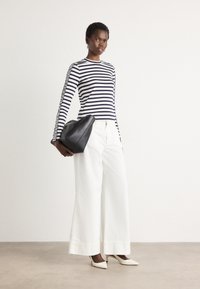 Maglietta a righe a maniche lunghe in blu navy e bianco, abbinata a pantaloni bianchi a gamba larga e décolleté bianche a punta, mentre tiene una borsa nera.