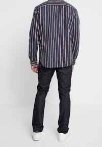 Marinblå och vit randig långärmad tröja kombinerad med mörka jeans och vita sneakers; synliga sömmar och knappdetaljer på ärmarna.