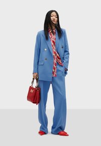 Light blue tailored suit with a double-breasted blazer, wide-leg pants, patterned multicolor shirt, red handbag, and red pointed shoes.