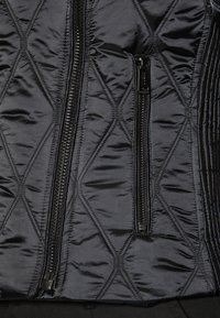 Black quilted jacket with diagonal stitching, featuring two zippered pockets and a smooth texture. Zippers have a matte finish.