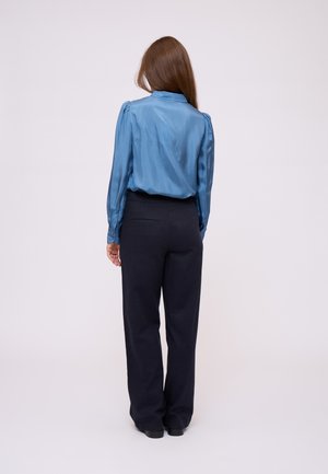 Zijdeblauwe blouse met opgesmukte mouwen, gecombineerd met zwarte high-waisted broeken. De outfit heeft een soepele textuur en een getailleerde pasvorm.