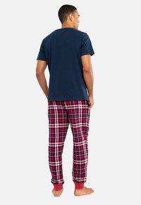 Marineblauwe katoenen t-shirt gecombineerd met rode en zwarte geruite pyjamabroek. De broek heeft elastische boorden en een relaxte fit.