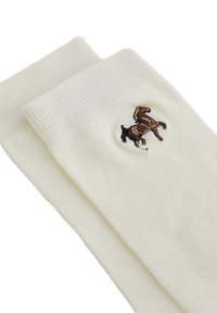 Calcetines color crema con textura acanalada, presentan un logo de caballo bordado en marrón en un lado. Tejido suave, longitud estándar de caña.