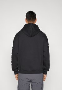 Camisola com capuz preta, tecido macio, corte descontraído, punhos e bainha canelados, capuz grande, design minimalista sem logótipos ou padrões visíveis.