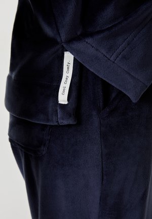 Marineblauwe fleece stof met een gestructureerd oppervlak. Inclusief een zijzak en een label met de tekst "Cool Cosy Comfy."