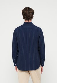 Tengerészkék, hosszú ujjú ing, függőleges csíkokkal, gombos mandzsettával, széles gallérral és egyenes aljjal. Hátsó nézet látható.