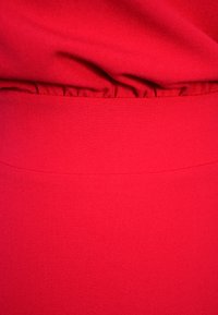 Czerwona tkanina o gładkiej teksturze. Posiada marszczenie w talii. Prosty design bez dodatkowych wzorów lub akcentów.