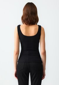 Zwart geribbelde tanktop met brede schouderbanden, aansluitend ontwerp en een ronde rug. Niet-geprofileerde, gladde stof. Gecombineerd met zwarte jeans.
