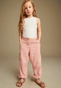 Vit ribbad linne som är kombinerad med rosa linne cargo-byxor. Sandaler med dekorativ guldaccent fulländar outfitet. Långt, vågigt hår.