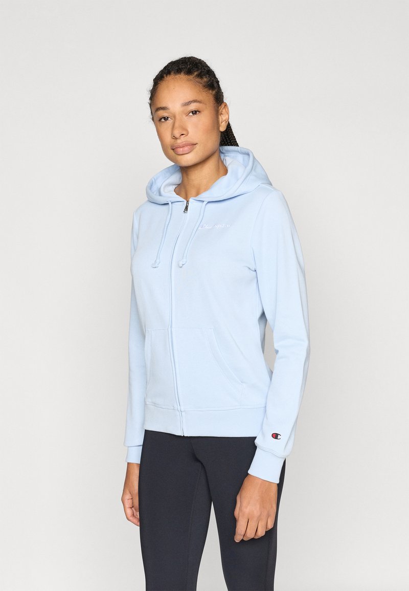 Φωτεινό γαλάζιο φούτερ με φερμουάρ, εμπρόσθια τσέπη, κουκούλα με κορδόνια και κεντημένο λογότυπο. Διαθέτει εφαρμοστά μανσέτα και απλή υφή.