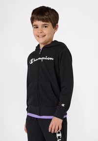 Felpa nera con zip frontale, con logo "Champion" bianco sul petto, tasche frontali e un piccolo logo sulla manica.