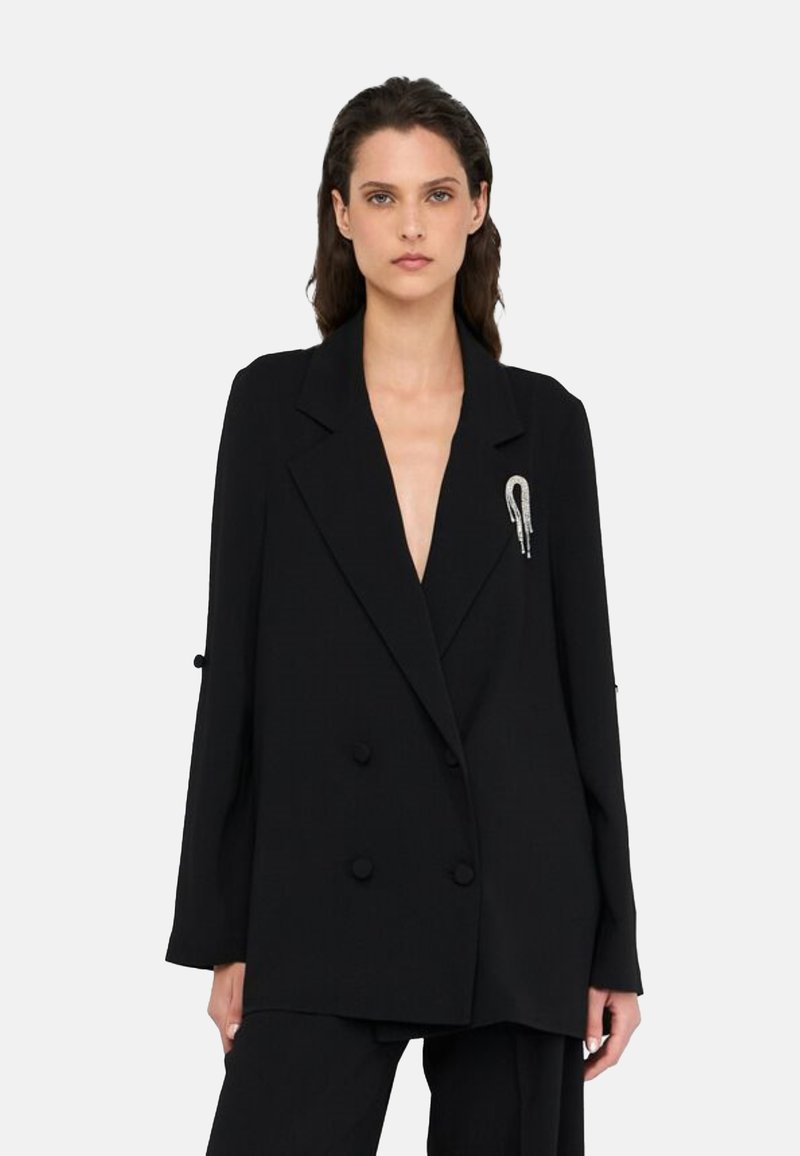 Blazer nero doppiopetto con maniche lunghe, tessuto strutturato e distintivo spillo d'argento sul petto a sinistra.