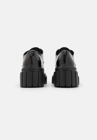 Chaussures en cuir verni noir avec semelles épaisses à plateforme striée, vues de dos sur un fond blanc.