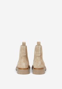 Bottines en daim couleur beige clair avec des panneaux latéraux élastiques, des languettes de talon côtelées et des semelles en caoutchouc texturées. Design simple avec un branding subtil.