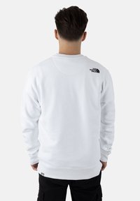 Sudadera blanca de manga larga, con puños y banda inferior acanalados. Presenta un pequeño logotipo negro en la parte superior de la espalda. Textura suave, diseño casual.