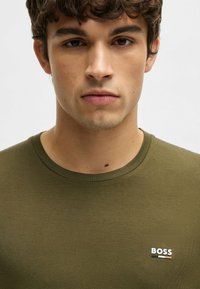 Olijfgroen T-shirt met korte mouwen van soepele, lichte stof. Bevat een klein wit 'BOSS' logo op de borst. Ronde halslijn.