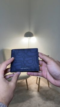 Dark blue wallet with a textured logo pattern, featuring a leather exterior and a metallic brand name, held in hands against a neutral background.