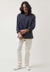 Camisa de lino azul marino con cuello estructurado, mangas largas y corte relajado, combinada con pantalones blancos con vuelta y zapatos blancos.