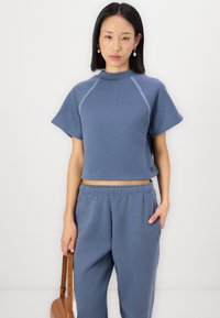 Blaues kurzes Sweatshirt mit kurzen Ärmeln, Raglan-Nähten und strukturiertem Stich. Kombiniert mit passenden blauen Jogginghosen, lässig getragen.