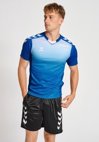 Blå gradient sports trøje med et geometrisk mønster, korte ærmer og v-hals. Kombineret med sorte shorts med hvide chevron-detaljer.