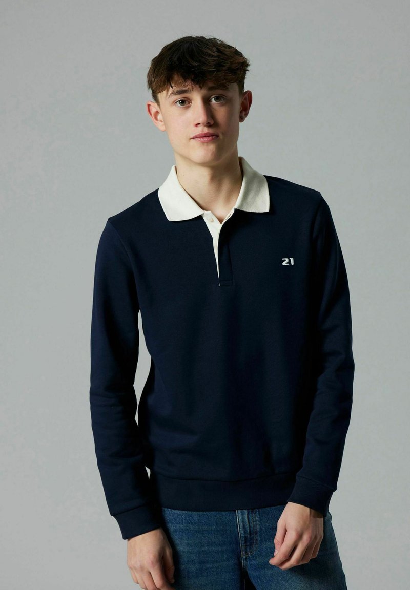 Maglione blu navy con colletto bianco, maniche lunghe e pattina frontale. Presenta un piccolo logo sul petto e polsini e orlo a coste.