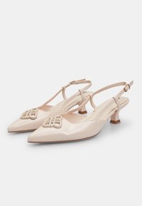 Bež lakirne slingback pete s špicastim nosom, nizkim blok petam in dekorativno detajlno zanko spredaj. Gladka tekstura.