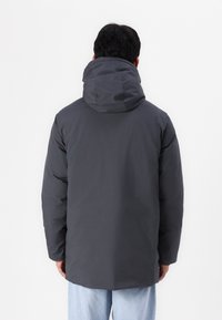 Grå isoleret jakke med hætte, der har en glat tekstur, lige nederste kant og en afslappet pasform. Bagfra viser den rene linjer og minimalistisk design.
