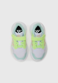 Baskets de sport blanches et vert menthe avec un dessus en maille, accents vert fluo, sangle réglable et semelle intérieure noire avec motif à rayures.