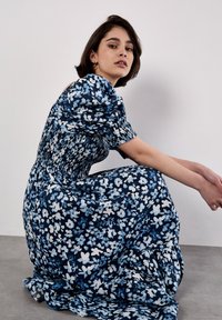 Robe florale en tissu bleu marine avec des motifs blancs et bleu clair. Présente un corsage froncé, des manches bouffantes et une jupe fluide.