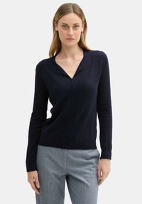 Marineblauer Strickpullover mit V-Ausschnitt und langen Ärmeln, der ein dezentes strukturiertes Muster und eine figurbetonte Silhouette aufweist.