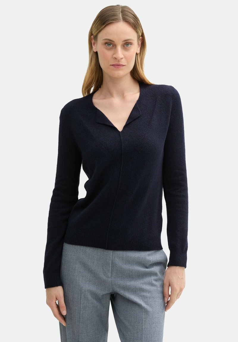 Marineblauer Strickpullover mit V-Ausschnitt und langen Ärmeln, der ein dezentes strukturiertes Muster und eine figurbetonte Silhouette aufweist.