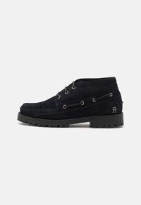 Botas de ante azul marino con un perfil bajo, punta redonda y superficie texturizada; cuentan con ojetes de metal y una suela negra dura.