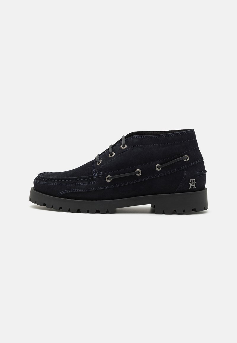 Botas de ante azul marino con un perfil bajo, punta redonda y superficie texturizada; cuentan con ojetes de metal y una suela negra dura.