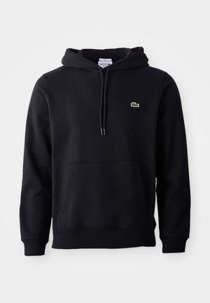 Zwarte capuchontrui met voorzak en klein groen krokodillenlogo op de linkerbout, afgebeeld op een witte achtergrond.