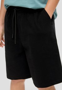 Zwarte katoenen shorts met een elastische tailleband, verstelbaar trekkoord en zijzakken. Zachte textuur, knielange ontwerp, minimale details.