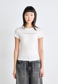 Bílý bavlněný tričko s černým logem "TOMMY JEANS" na hrudi, krátkými rukávy a klasickým kulatým výstřihem.