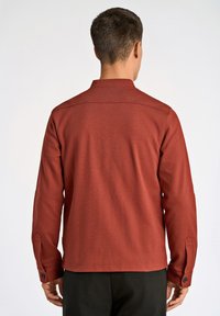 Röd långärmad skjorta med krage, utrustad med knappribbor och en slät textur. Baksidan visar en ren, enkel design.