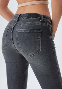 Jeans de mezclilla gris con un diseño ajustado, que cuentan con bolsillos traseros, sutiles detalles de costura y una etiqueta de cuero de marca en la cintura.