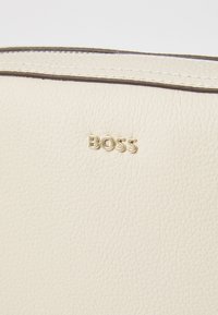 Borsa in pelle color crema con superficie texture, logo dorato "BOSS" e bordo in contrasto scuro lungo i lati.
