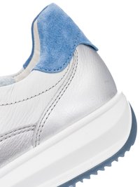 Close-up of sneaker heel with white leather, blue suede accent, detailed stitching, and thick white sole with blue tread.