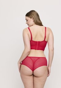 Un reggiseno in pizzo rosso e un perizoma coordinato presentano pattern intricati, spalline regolabili e una consistenza morbida, evidenziando un design aderente.