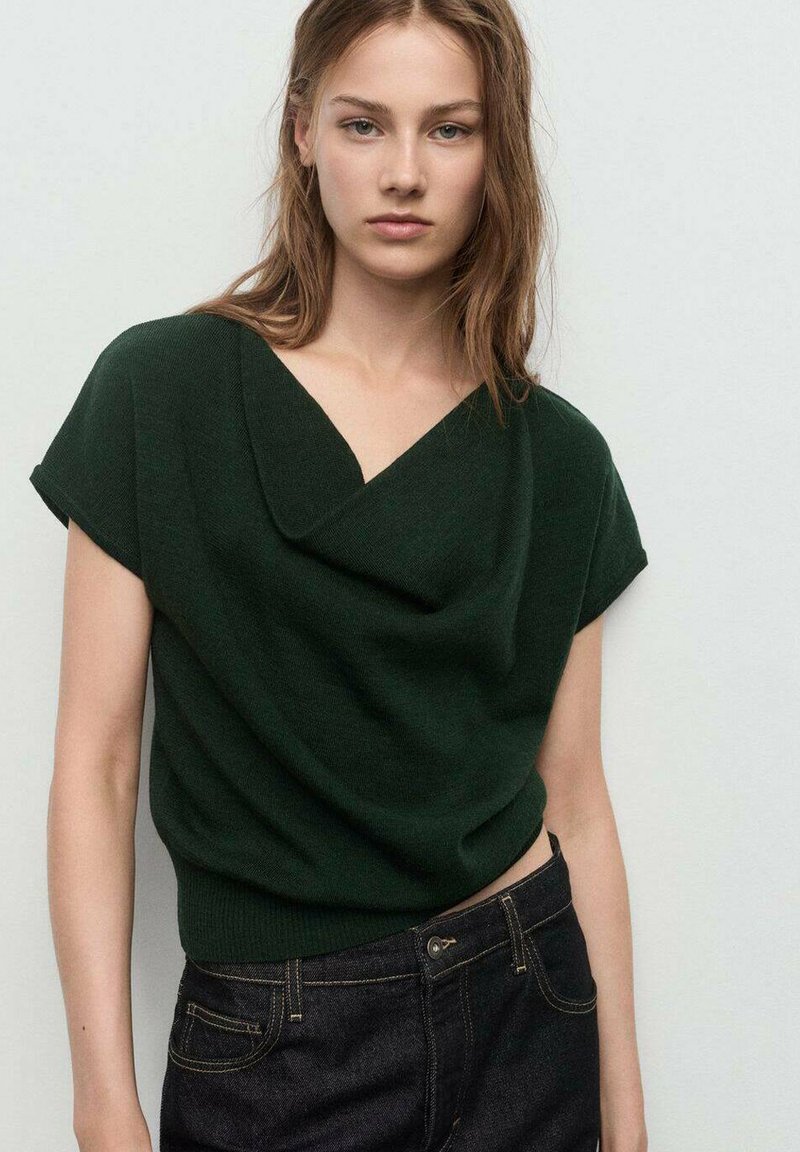 Top verde lavorato a maglia con scollatura drappeggiata, maniche corte e orlo aderente, abbinato a jeans in denim scuro. Design semplice senza fantasie.