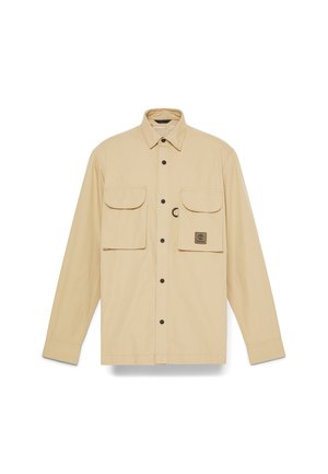 Beige langemouwen shirt gemaakt van lichtgewicht stof, met twee borstzakken met knoopsluitingen en een logo flap op de linkerzak.