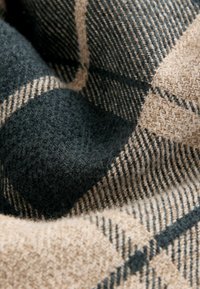 Wollstoff in Dunkelgrün und Beige, mit einem klassischen Karomuster, das unregelmäßige Texturen und kontrastierende Linien aufweist.