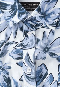 Chemise pour homme à col avec boutons, grand motif floral bleu et blanc et étiquette de marque visible à l'intérieur du col.