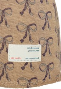 Kangas helepruuni taustaga, millel korduv mustriga tumepruunide ja sinakashallide vibu kujund. Sisaldab valget kangasildiga, millel on tekst.