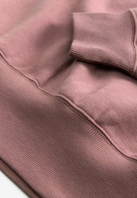 Close-up van een stoffige roze sweatshirt-manchet en tailleband die de zachte, geribbelde breistructuur en gedetailleerd stiksel op gladde stof tonen.